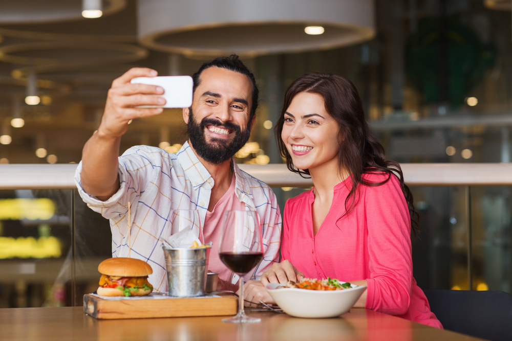 Hispanic couple taking selfie with smartphone and and using Snapchat in a restaurant