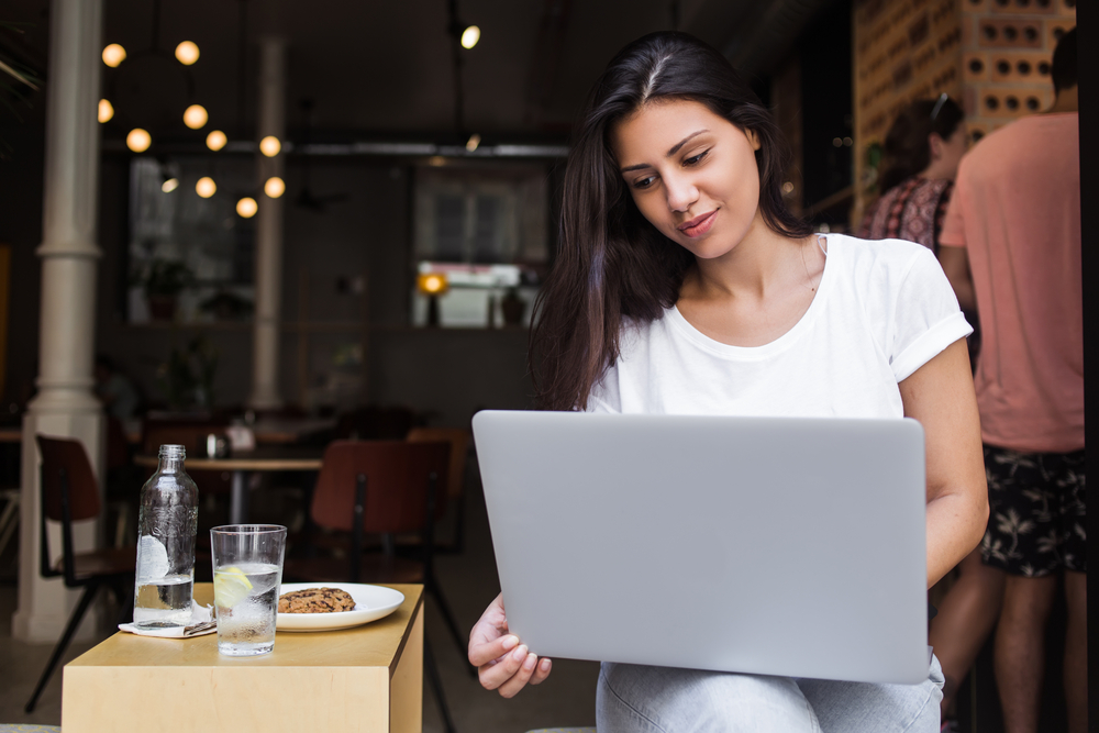 Mujer joven con laptop en cafetería tomando uno de los cursos de negocios en línea